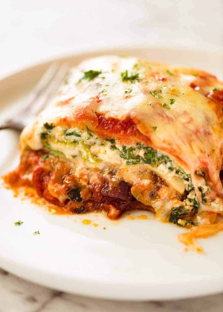 a white plate topped with lasagna covered in sauce and cheese next to a fork