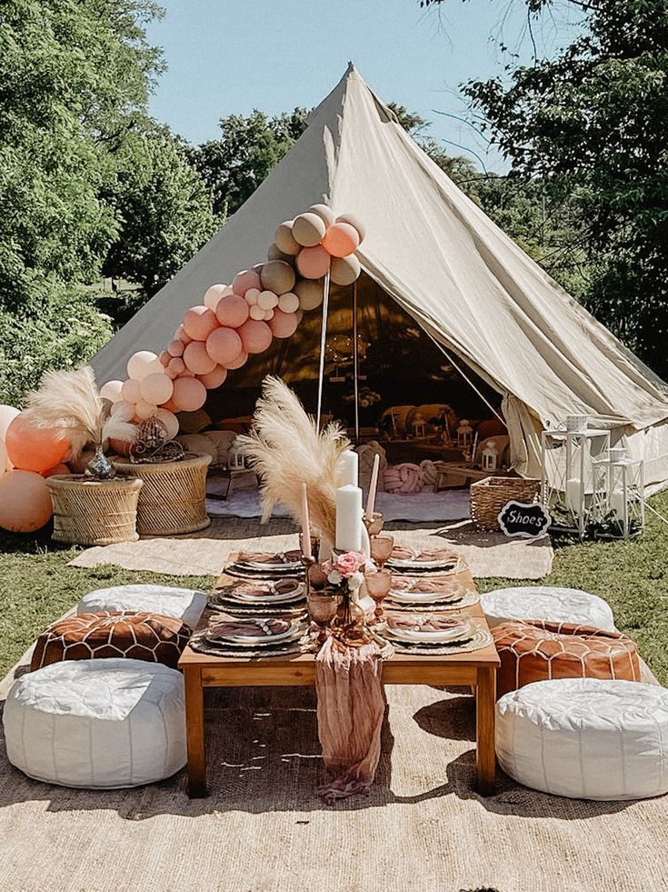 an outdoor tent set up for a party with balloons and pillows on the ground,