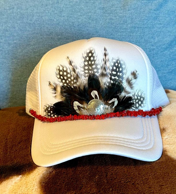 This beautiful white trucker hat with black & white colored feathers, a silver buffalo nickel concho embellishment, and a removable red stone hat band will be all anyone can talk about when you wear it.  It's such a fun way to spice up any outfit and the places to wear this hat are endless. Be prepared for loads of compliments.  The feathers are handpicked for each hat.  The hat has a foam front, mesh back, and an adjustable snap back. Colored Feathers, White Trucker Hat, Coloured Feathers, Buffalo Nickel, Hat Ideas, Castle Rock, Snap Back, Hat Band, Red Stone