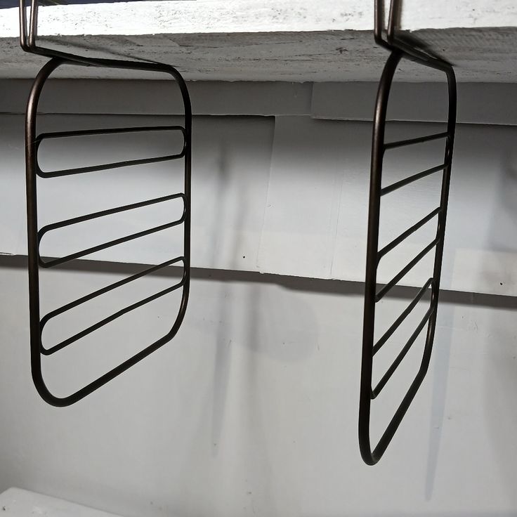 two metal racks hanging from the side of a window sill next to a white wall