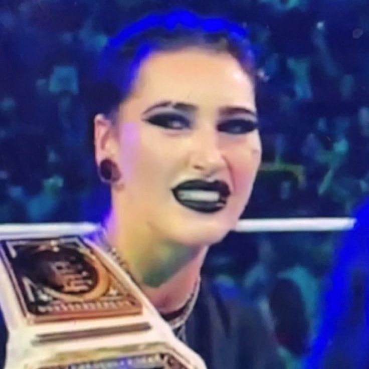 a woman with black makeup holding up a wrestling belt