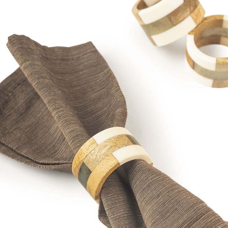 two napkin rings are sitting on top of a brown cloth with gold and white bands