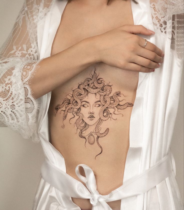 a woman with a tattoo on her stomach wearing a white robe and holding onto the side of her body