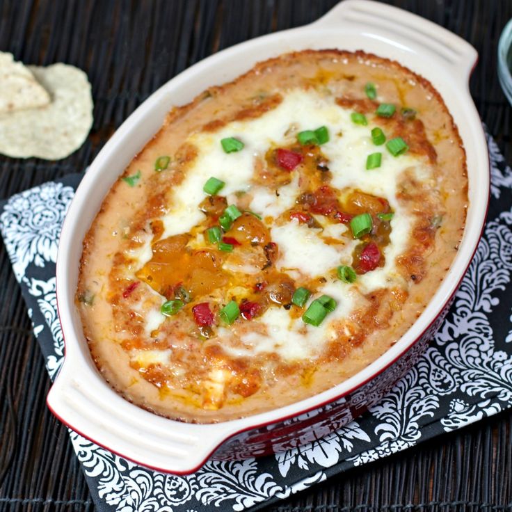 an oval casserole dish with cheese, bacon and green onions in it next to crackers