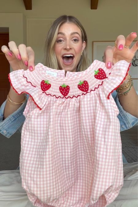 a woman is holding up her baby's pink gingham dress with strawberries on it