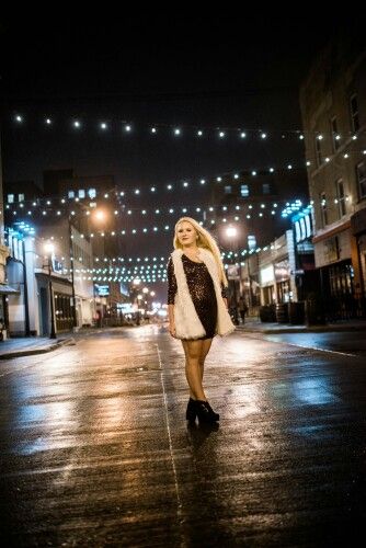 a woman is walking down the street at night wearing a fur vest and black boots