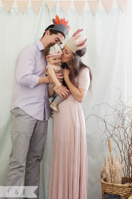 a man and woman standing next to each other in front of a white backdrop holding a baby