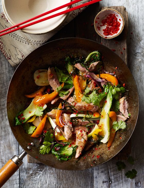 a bowl filled with meat and vegetables next to chopsticks on a wooden table