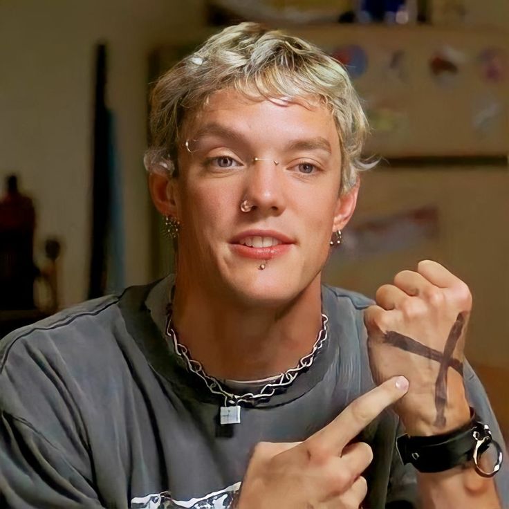 a man with glasses and a cross on his wrist is making a gesture to the camera