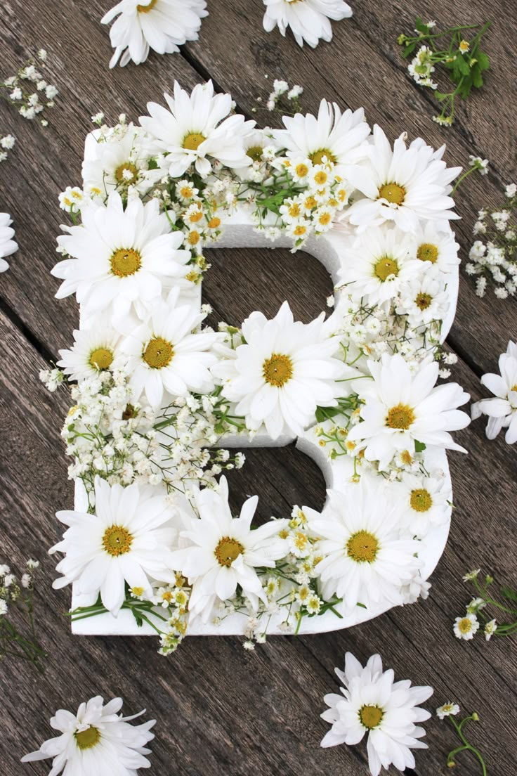 the letter b is made up of daisies and other wildflowers on a wooden surface