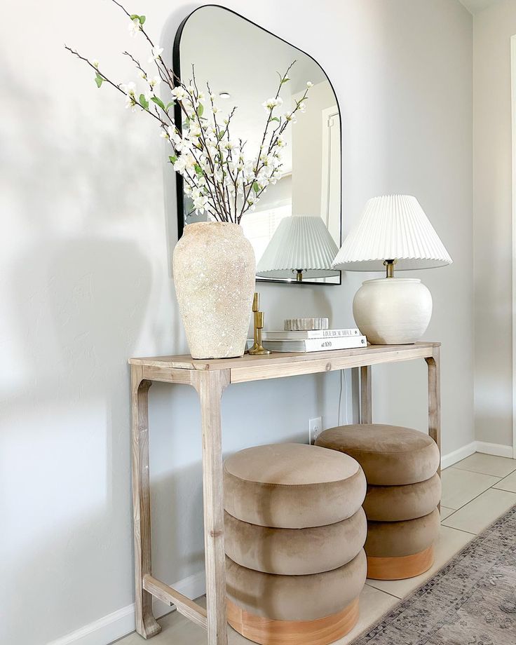 a white vase sitting on top of a wooden table next to a mirror and stool