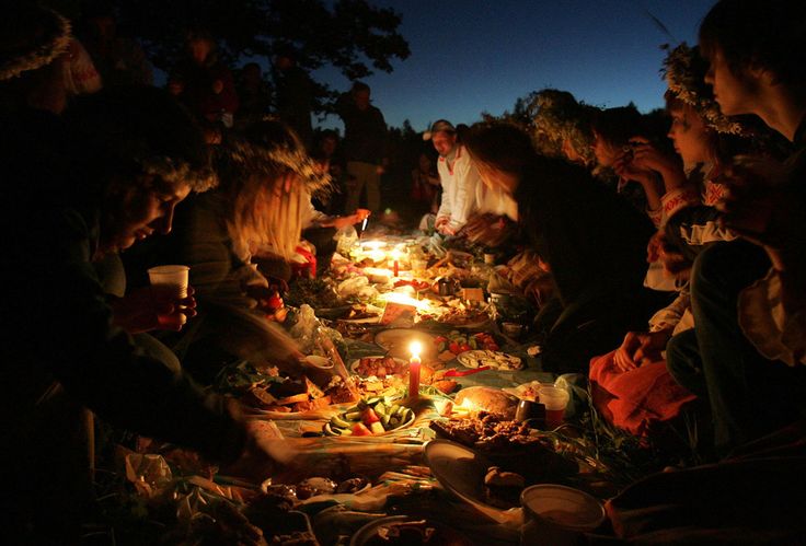 a group of people sitting around a table with food and candles on it at night