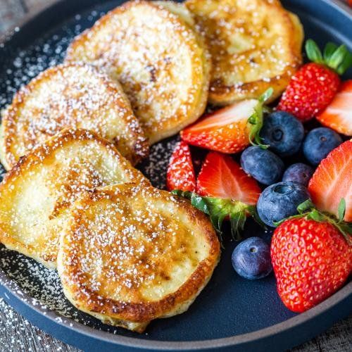 french toast with berries and powdered sugar on a blue plate next to strawberries