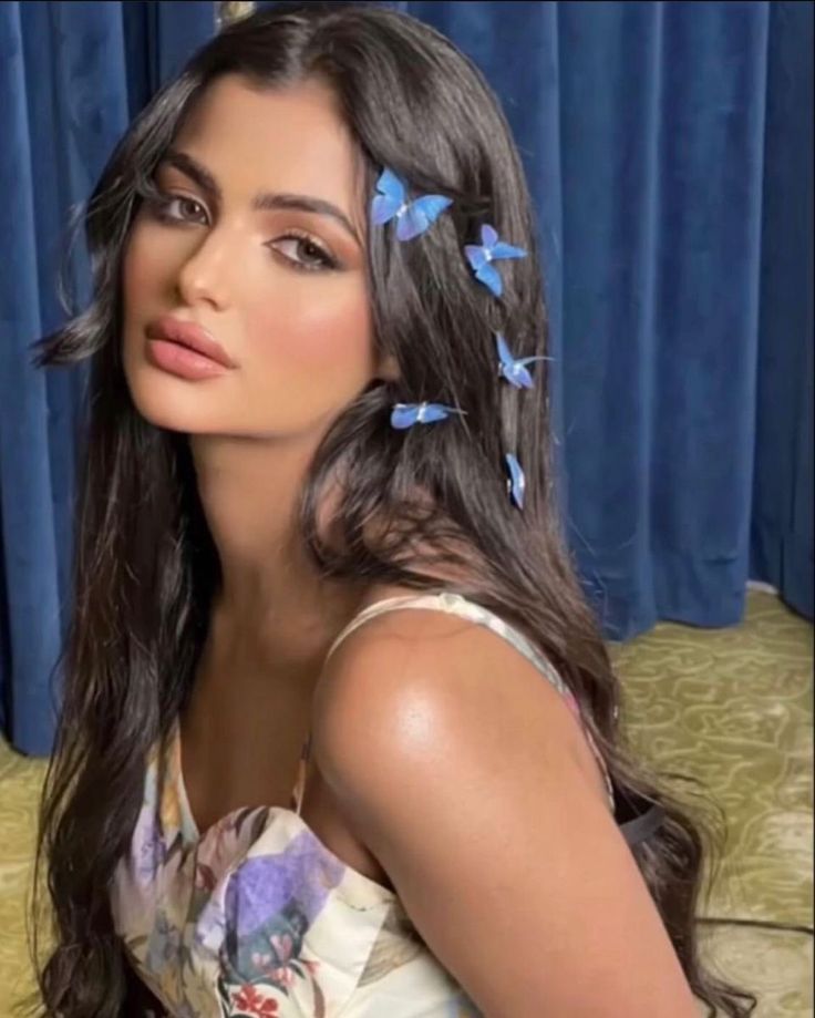 a woman with long dark hair and blue butterflies in her hair sitting on a couch