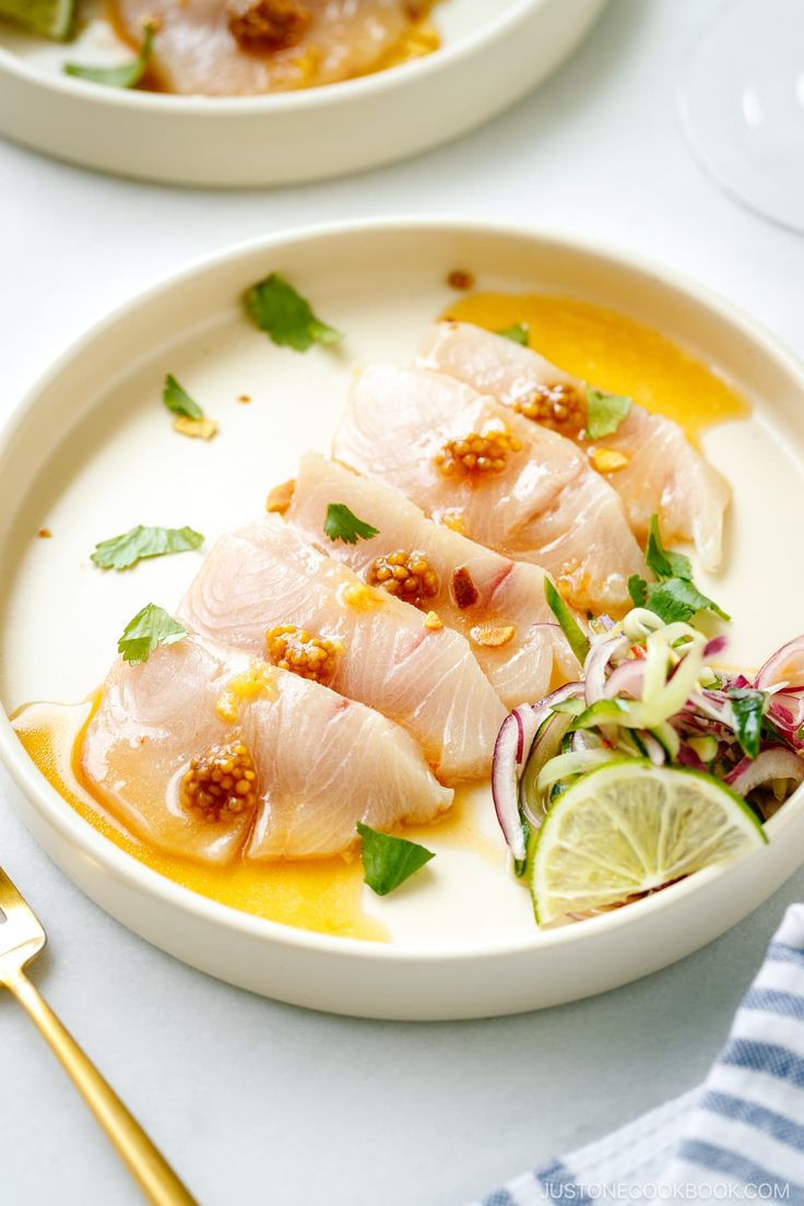 two white plates with food on them and gold utensils next to each other