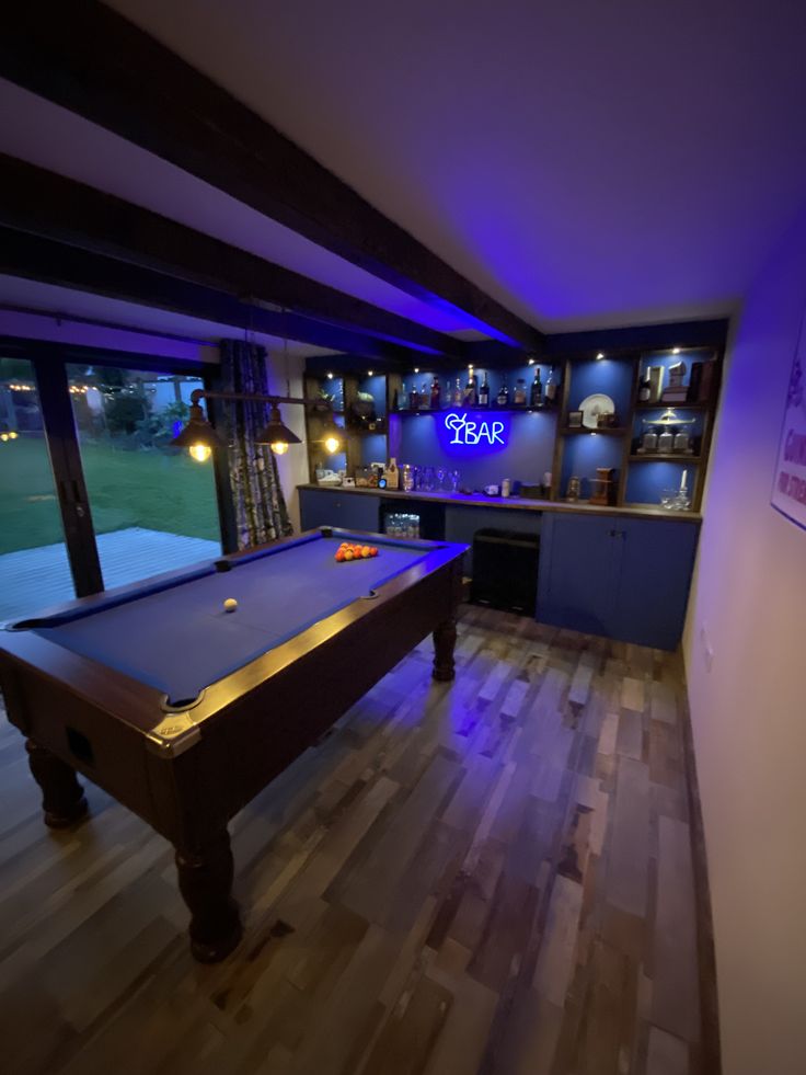 a pool table in the middle of a room with blue lights on it and a bar behind it