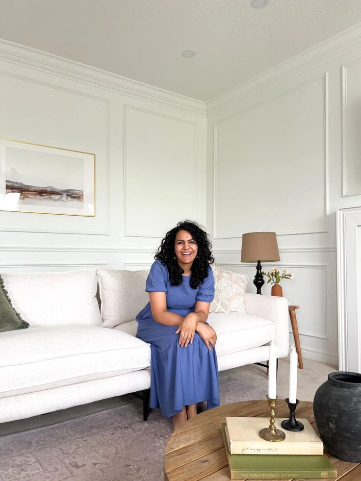 a woman in a blue dress sitting on a white couch next to a coffee table