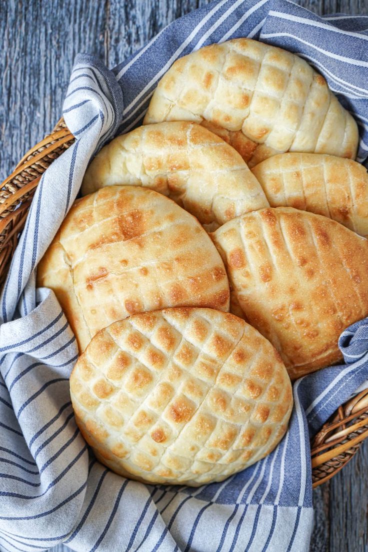 some breads are in a basket on a wooden table with a blue and white towel