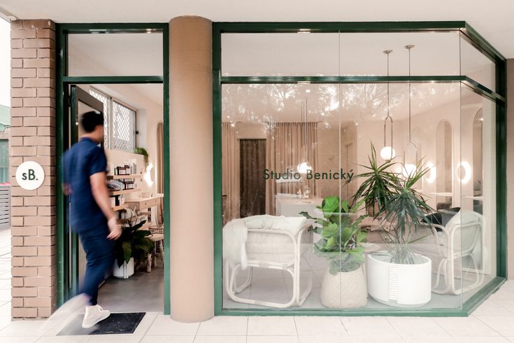 a man is walking in front of a store window with plants and chairs on display