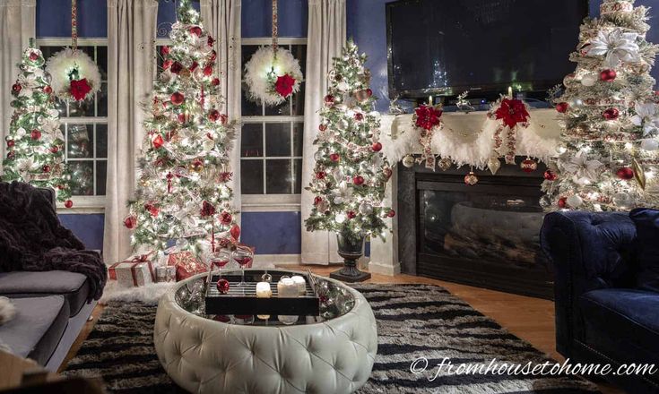 a living room decorated for christmas with white and red decorations on the tree, blue couches and fireplace