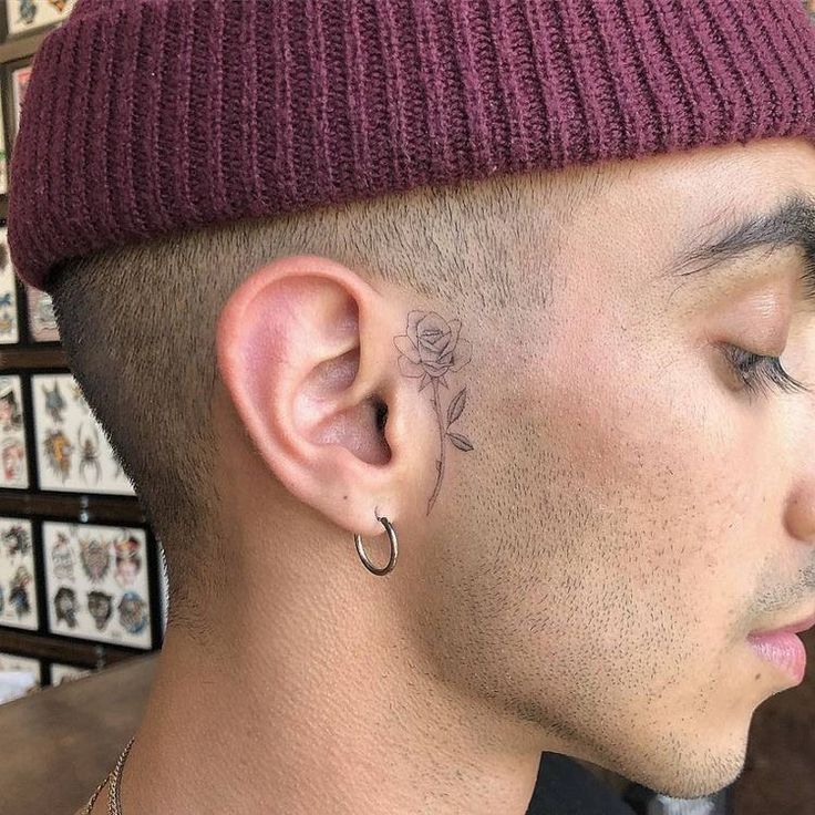 a young man with a flower tattoo on his left side of the ear, wearing a beanie