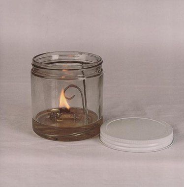 a glass jar with a lit candle in it next to a white lid on a table