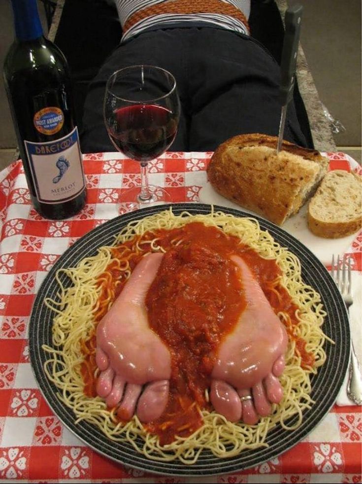 a plate with spaghetti and meat on it next to bread, wine glass and bottle