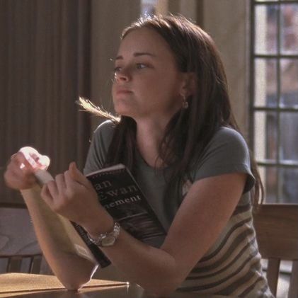 a woman sitting at a table with a book in her hand and looking up into the sky