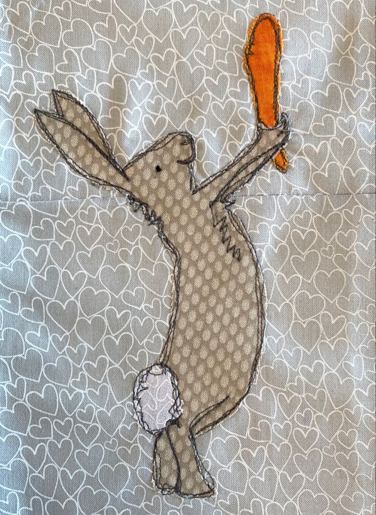 an embroidered rabbit holding a carrot in its paws on a gray and white patterned background