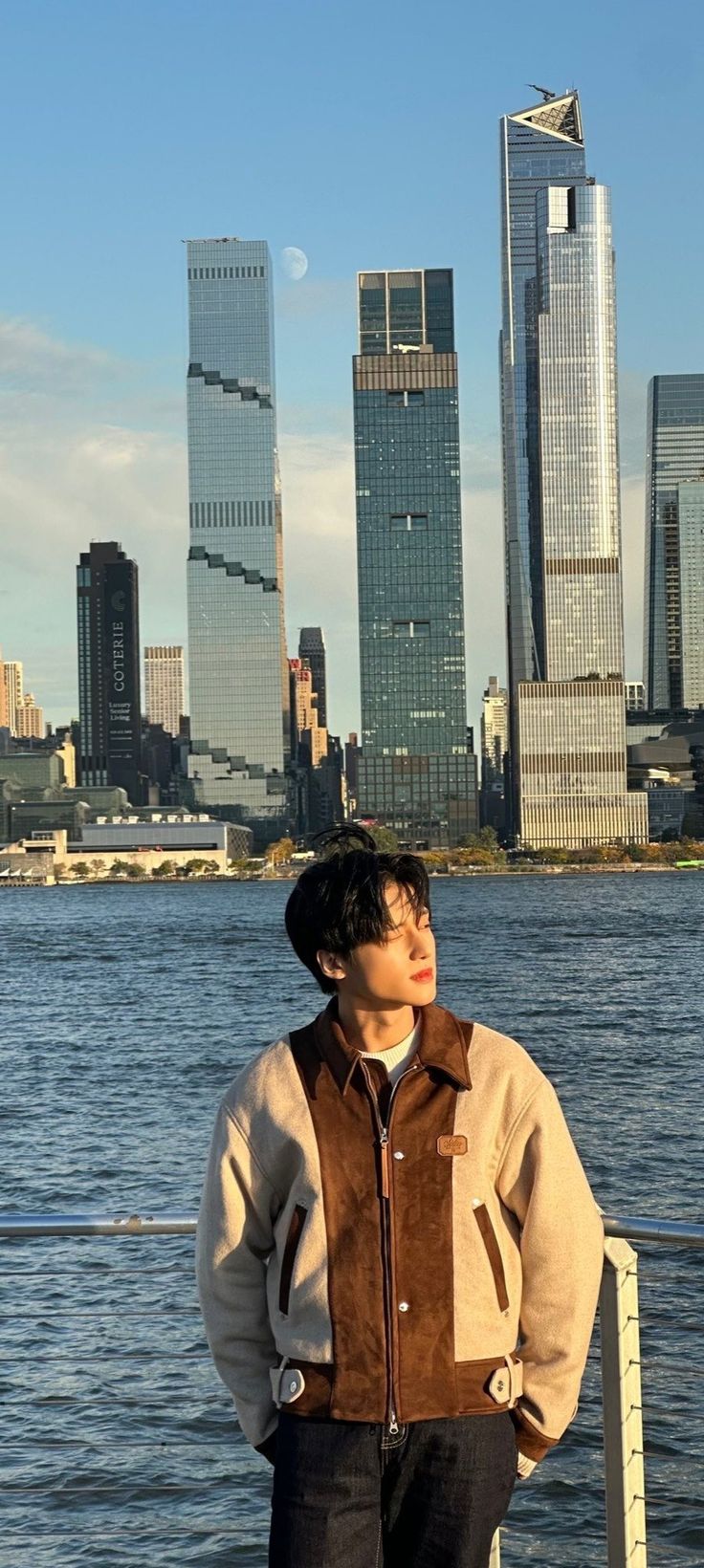 a man standing next to the water in front of some tall buildings and skyscrapers