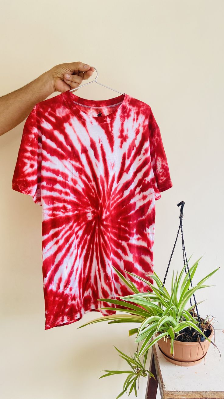 a red and white tie - dyed shirt hanging on a clothes line next to a potted plant