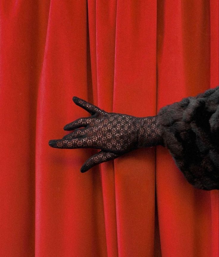 a woman's hand on top of a red curtain with black lace gloves over it