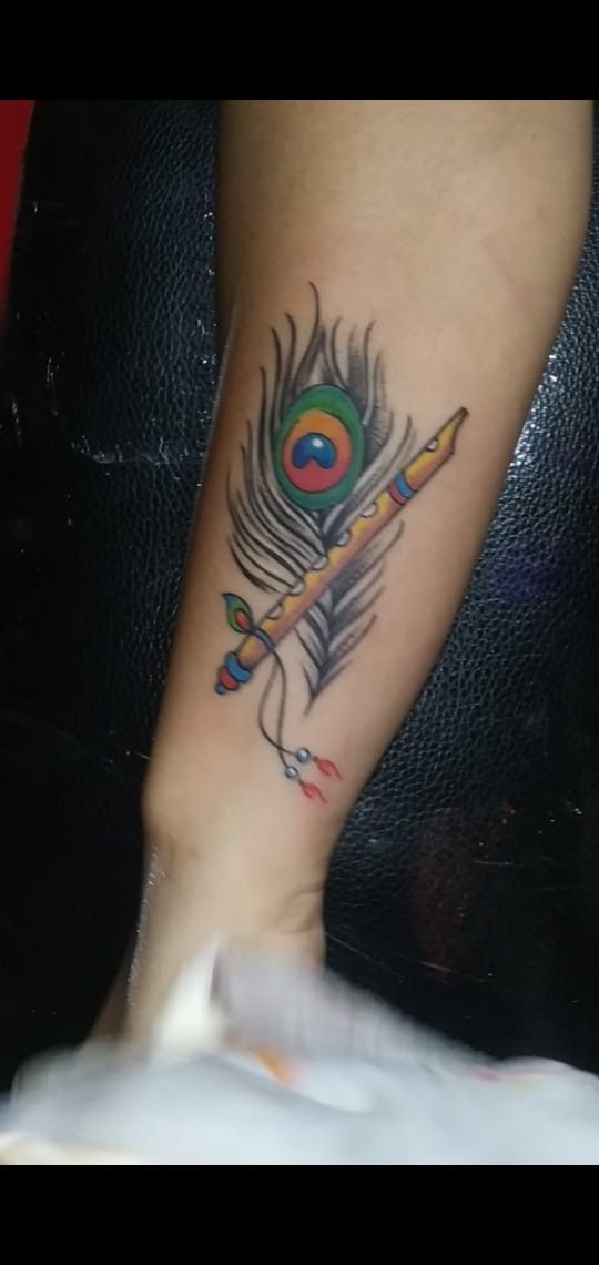 a woman's foot with a colorful feather and flute tattoo on her left leg