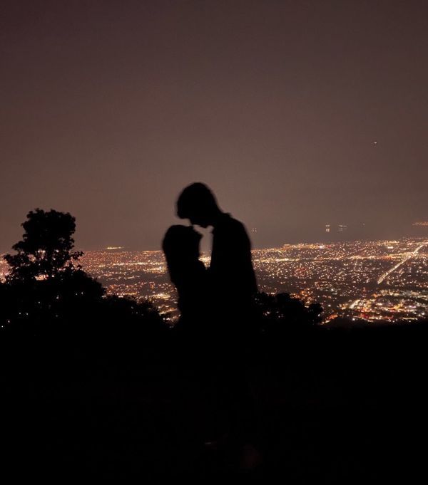 a person sitting on top of a hill at night with the city lights in the background