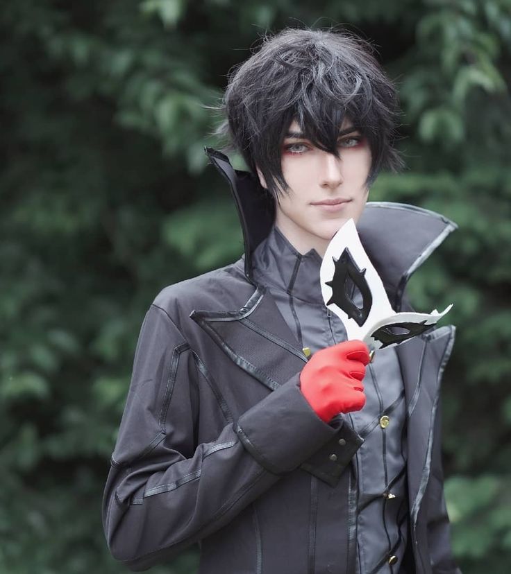 a man with black hair and red gloves holding scissors in front of his face while standing next to trees