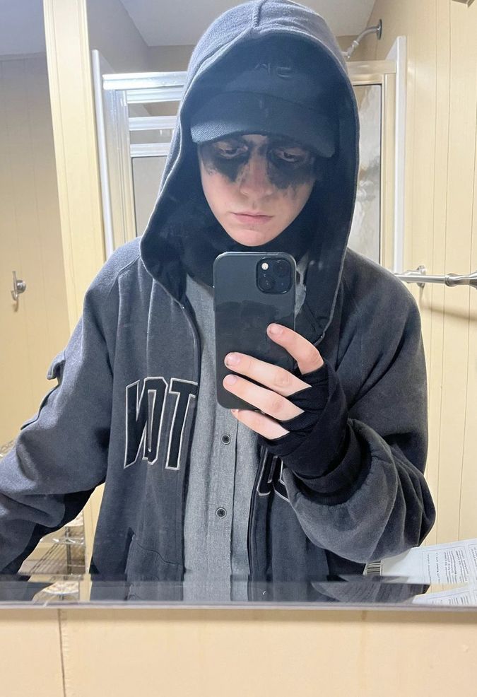 a man in a hoodie taking a selfie with his cell phone while standing in front of a mirror