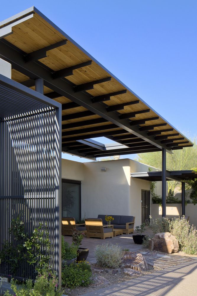 an outdoor covered patio area with furniture and plants on the side of the house, under a pergolated roof