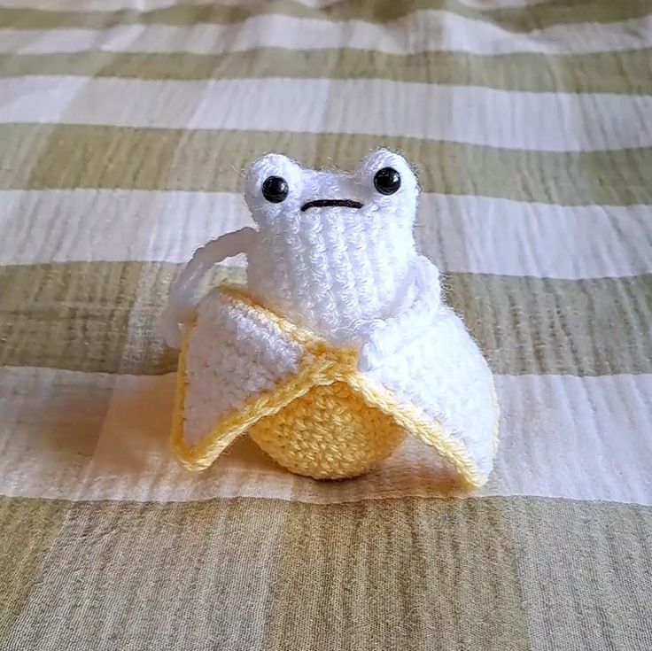 a crocheted frog sitting on top of a bed next to a banana peel