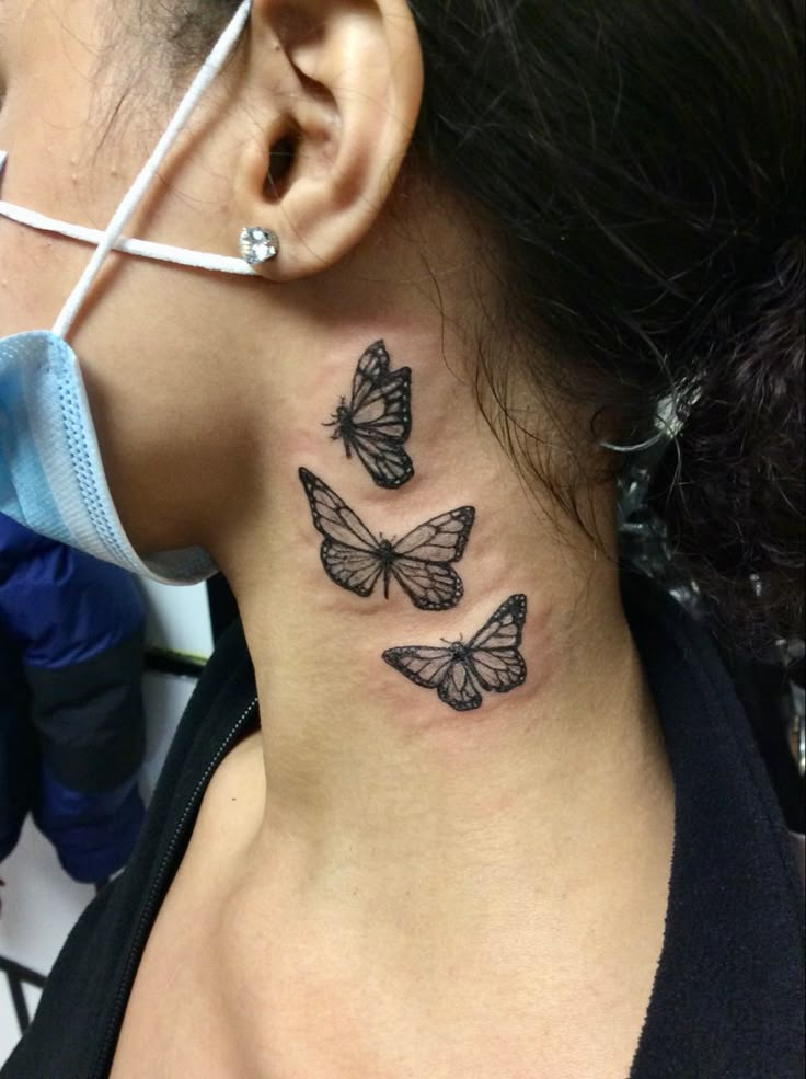 a woman's neck with three butterflies on her left side and behind her ear