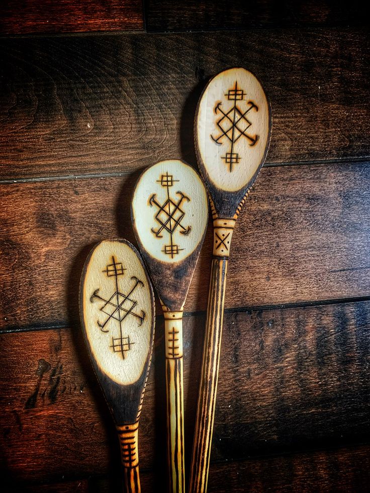 three wooden spoons with designs on them sitting on top of a wood floor next to each other