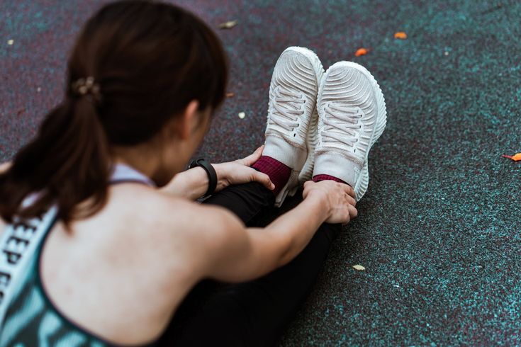 a woman sitting on the ground tying her tennis shoes