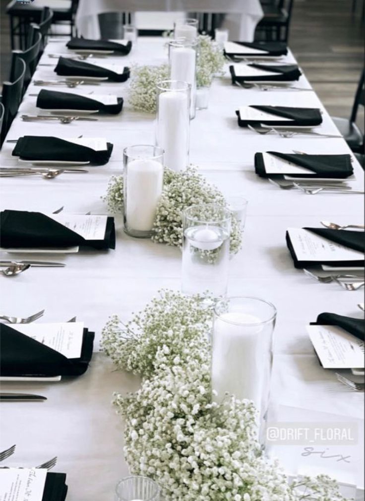 a long table is set with white flowers and black napkins for an elegant dinner