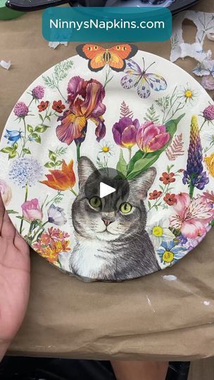 a paper plate with a cat on it and flowers painted on the front is being held by someone's hand