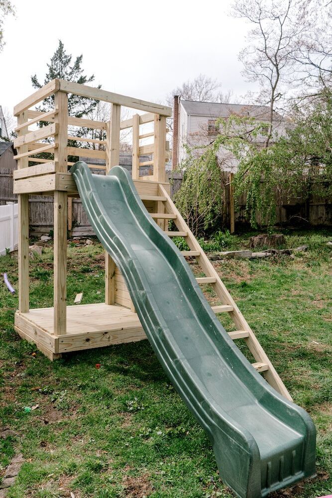 a green slide is in the grass next to a wooden structure