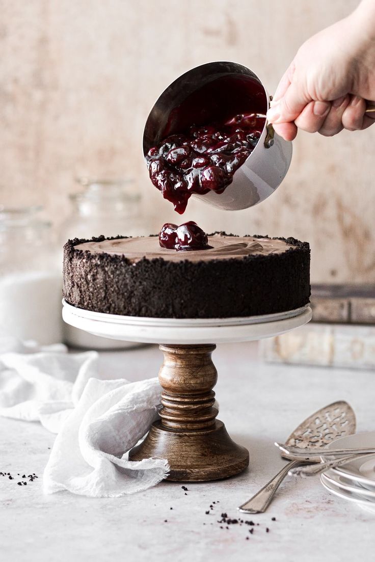 someone is spreading icing onto a chocolate cake with cherries on the frosting