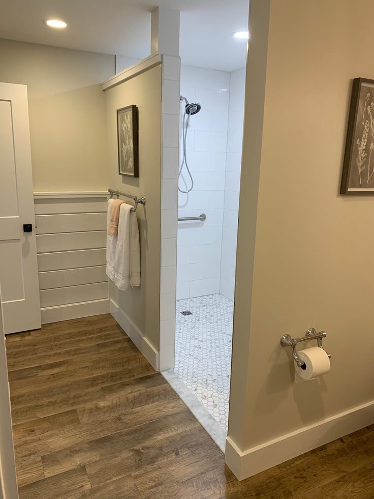 a bathroom with wood floors and white walls, including a walk - in shower next to a toilet