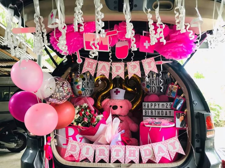 the trunk of a car decorated with pink and gold balloons, streamers, and decorations