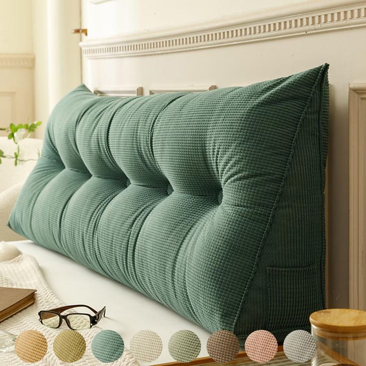 a green pillow sitting on top of a bed next to eyeglasses