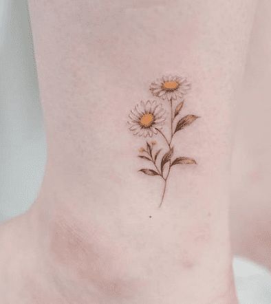 a woman's ankle with two daisies tattooed on the bottom of her foot