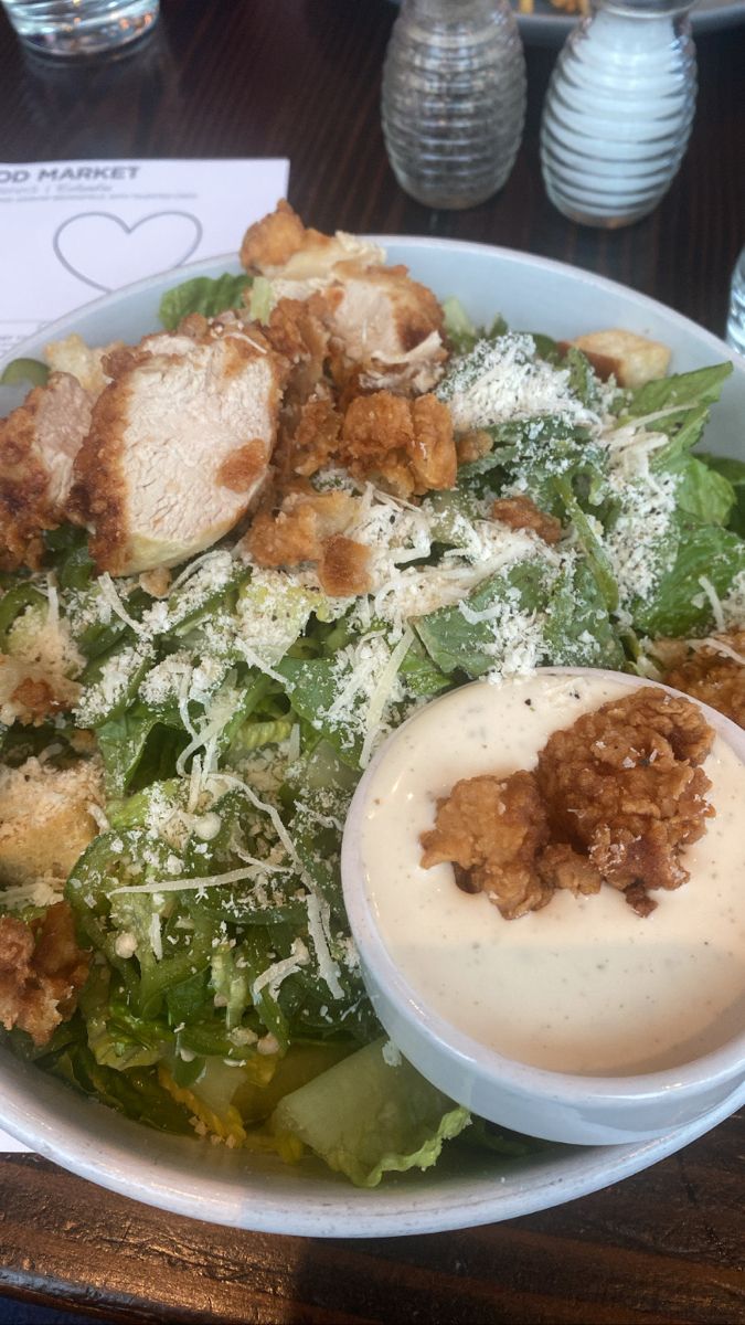 a salad with dressing in a white bowl on top of a wooden table at a restaurant